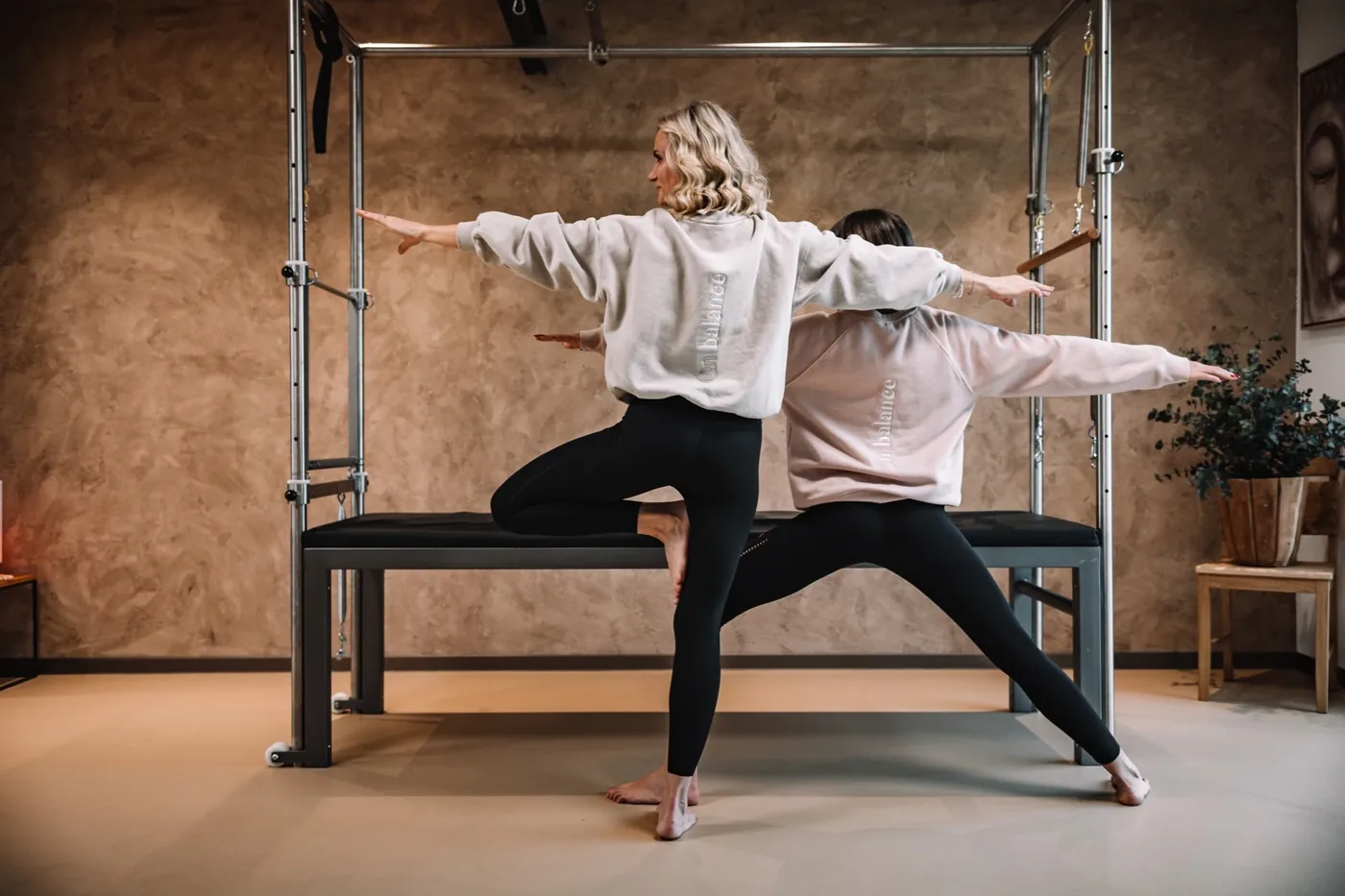 Dvě cvičenky v jógové pozici stromu před pilates cadillacem