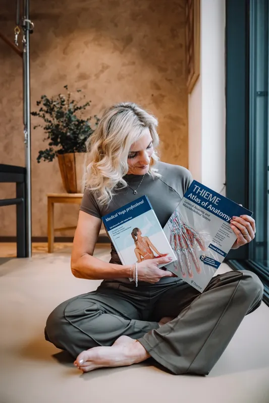 Lenka Vokřínková sedí na zemi a drží atlas anatomie a knihu Medical Yoga