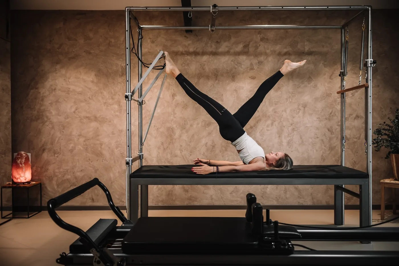 Cvičenka leží na pilates cadillacu s nohama zavěšenýma v popruzích