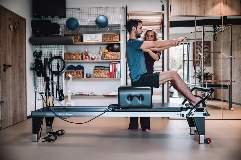 Lektorka vede klienta v sedu na pilates reformeru s napřaženýma rukama